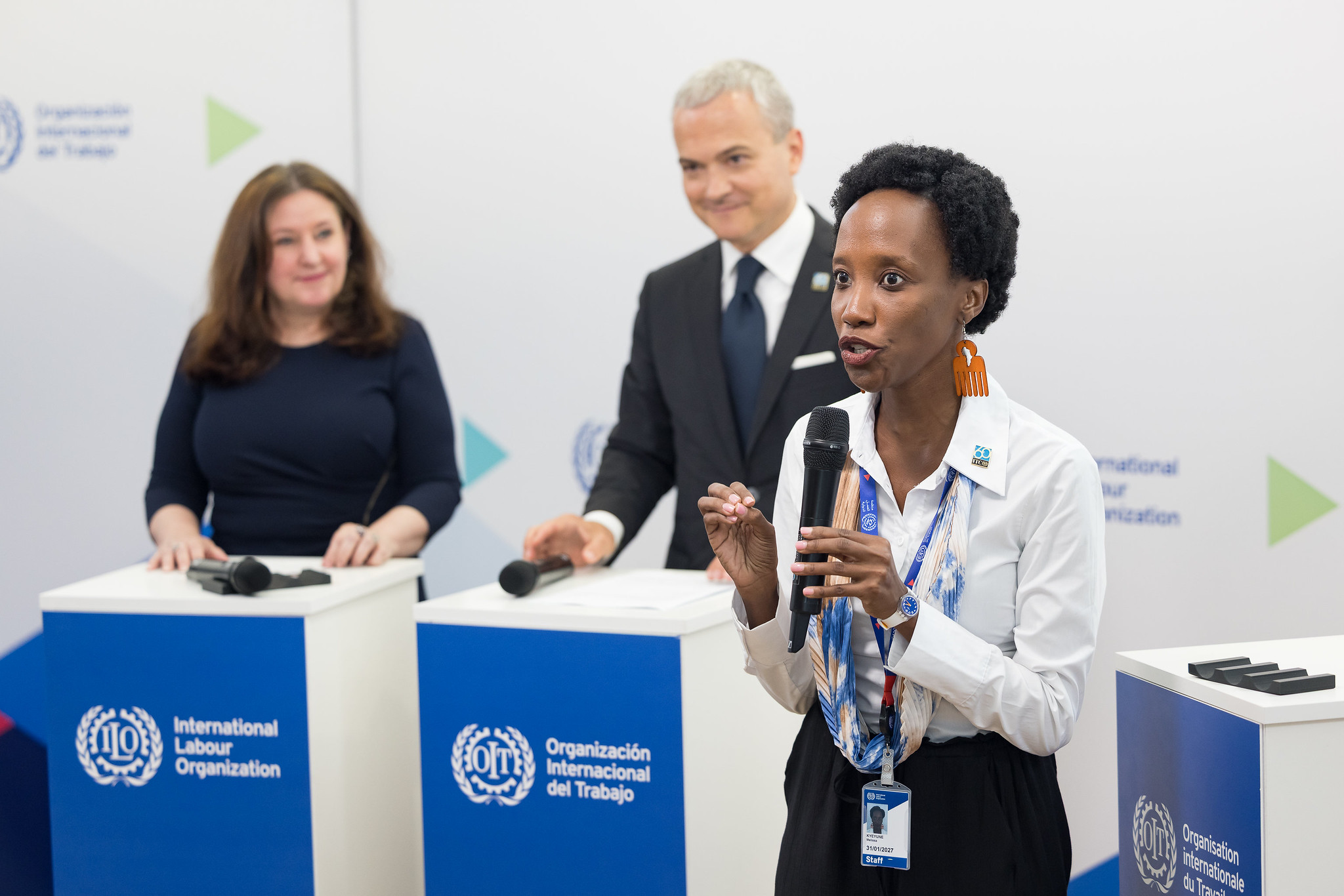Melissa Kyeyune tenant un microphone sur scène avec deux autres personnes debout derrière des podiums