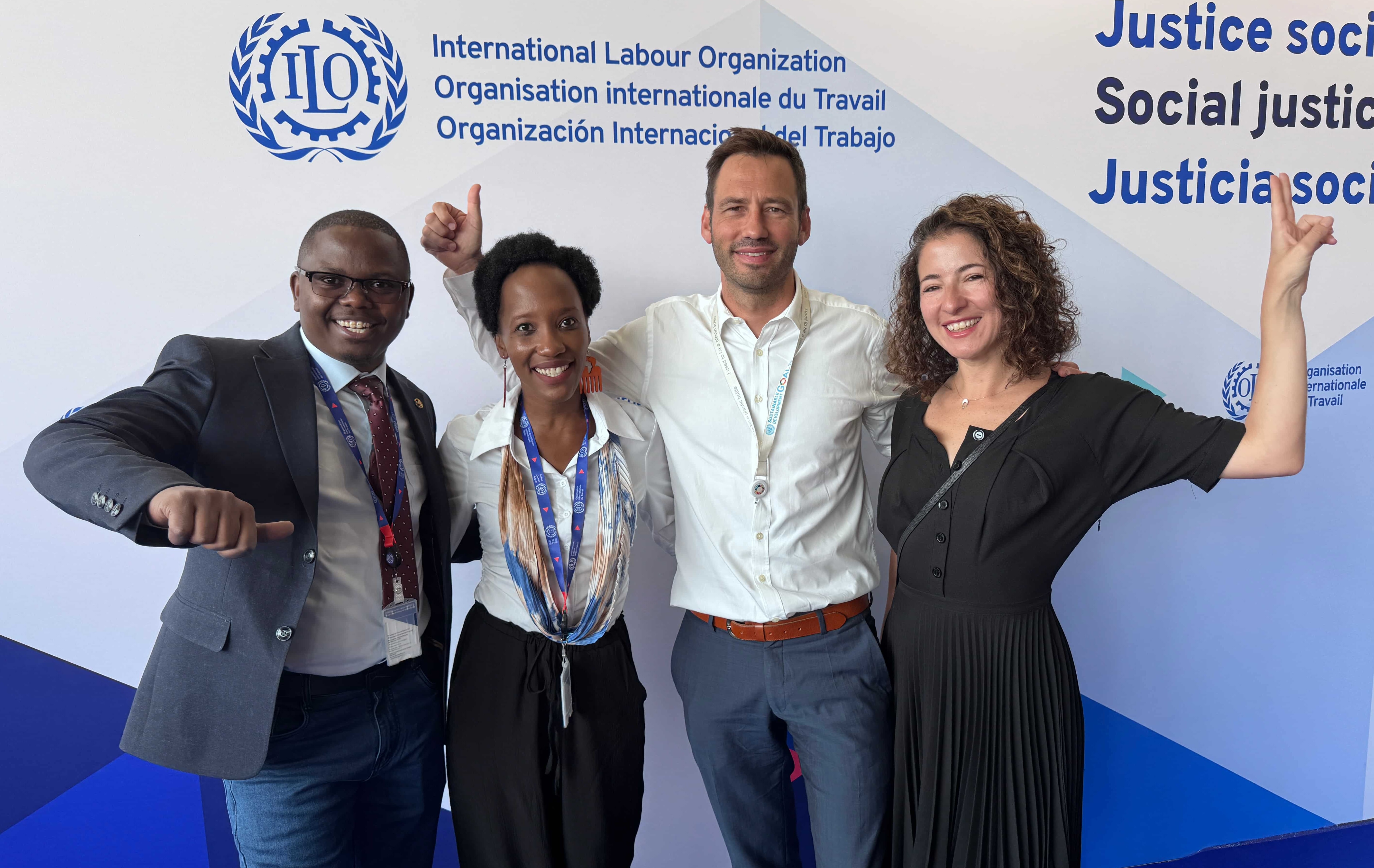 Stephen Muchiri Mwangi, Melissa Kyeyune, Rafael Peels and Cristina Maldonado standing together giving the thumbs up in front of an ILO backdrop